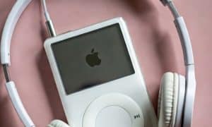 Professional 1:1 square studio photograph of the top profile of a silver Apple iPod Classic, focusing on the headphone jack socket against a solid light pink background for Atlantis repair services.