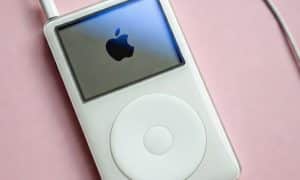 Professional 1:1 square studio photograph of an Apple iPod Classic with a bright, illuminated screen, set against a solid light pink background for Atlantis screen repair services.
