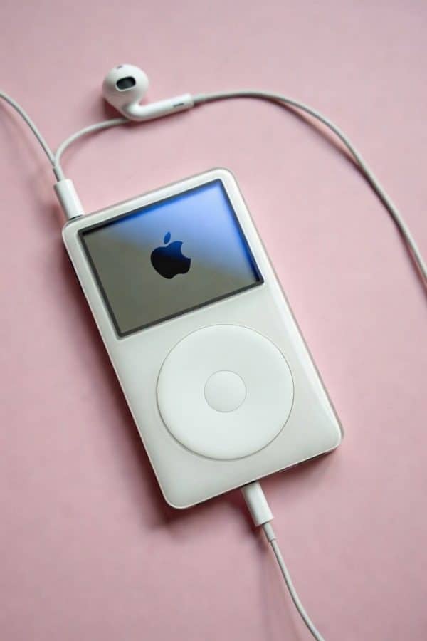 Professional 1:1 square studio photograph of an Apple iPod Classic with a bright, illuminated screen, set against a solid light pink background for Atlantis screen repair services.