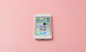 Professional 1:1 square studio photograph showing the bottom edge of a silver iPod Touch, focusing on the Lightning charging port against a solid light pink background for Atlantis repair services.