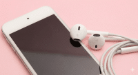 Professional studio photograph close-up of a white Apple iPod Touch with a pair of white earbuds resting on the screen, set against a solid light pink background for Atlantis specialised audio repair services