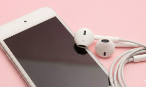 Professional studio photograph close-up of a white Apple iPod Touch with a pair of white earbuds resting on the screen, set against a solid light pink background for Atlantis specialised audio repair services