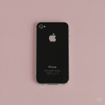 Close-up of the rear glass panel of an Apple iPhone 4, showcasing the smooth glass finish and Apple logo on a solid light pink background for Atlantis repair services.