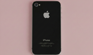 Close-up of the rear glass panel of an Apple iPhone 4, showcasing the smooth glass finish and Apple logo on a solid light pink background for Atlantis repair services.
