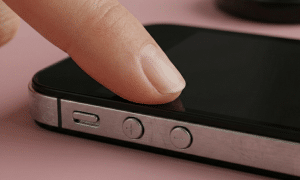 Close-up of the circular volume up and down buttons on the side of an Apple iPhone 4, set against a solid light pink background for Atlantis repair services.