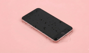 Professional studio photograph of a silver iPod Touch with water droplets on the black screen and sitting in a small puddle, set against a solid light pink background, representing liquid damage repair services at Atlantis.