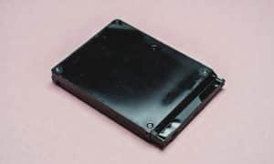 Professional studio photograph of a PlayStation 4 console with its internal components visible, featuring a new 1TB hard drive and a replacement Blu-ray laser lens assembly on a clean studio background