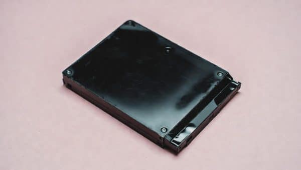 Professional studio photograph of a PlayStation 4 console with its internal components visible, featuring a new 1TB hard drive and a replacement Blu-ray laser lens assembly on a clean studio background