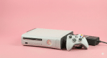 Professional studio photograph of a white original Xbox 360 console displaying the Red Ring of Death (RROD) error with three red lights on the power button, set against a light pink background.