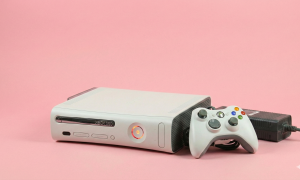 Professional studio photograph of a white original Xbox 360 console displaying the Red Ring of Death (RROD) error with three red lights on the power button, set against a light pink background.