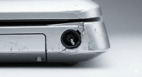 Close-up technical view of a broken DC charging port on a silver Sony Vaio laptop, showing a bent internal pin and cracked casing, isolated on the Atlantis signature studio background.