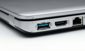 Close-up view of a physically damaged USB 3.0 port on a silver Sony Vaio laptop, showing a broken blue plastic tongue and bent metal casing, isolated on the Atlantis studio background.