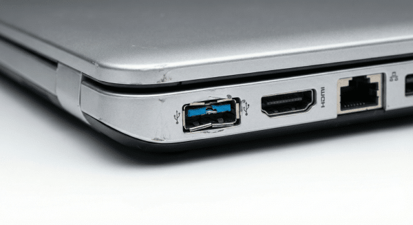 Close-up view of a physically damaged USB 3.0 port on a silver Sony Vaio laptop, showing a broken blue plastic tongue and bent metal casing, isolated on the Atlantis studio background.