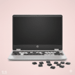Professional 1:1 square studio photograph of a silver HP laptop with several missing keys on the keyboard and loose keycaps resting on the light pink surface for Atlantis keyboard repair services