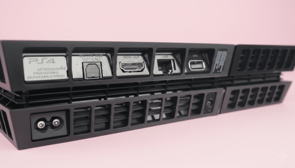 Professional 1:1 square studio photograph of the rear profile of a black PlayStation 4 console, highlighting the metal HDMI port against a solid light pink background for Atlantis console repair services.