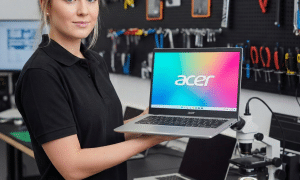 A professional technician using a microscope to identify and remove corrosion from an Acer Nitro motherboard after a liquid spill, shown on a solid light pink background for Atlantis repair services.