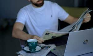 man sitting with newspaper over laptop